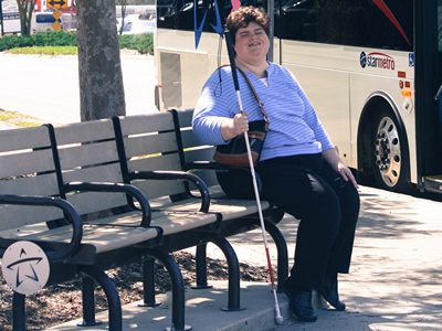 Blind woman holding a cane and waiting for a bus