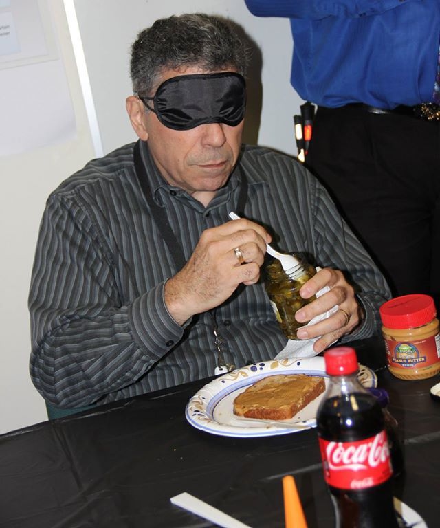 Man blindfolded while making a peanut butter and jelly sandwich 