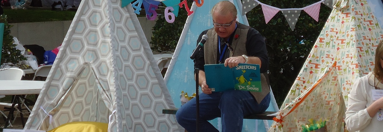 Steve Adams reads a book on stage to children