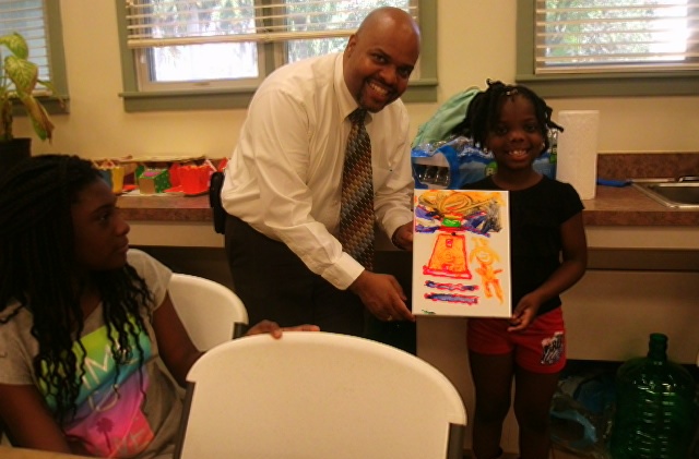 Director Robert Doyle and a young student smile while holding the student’s artwork.