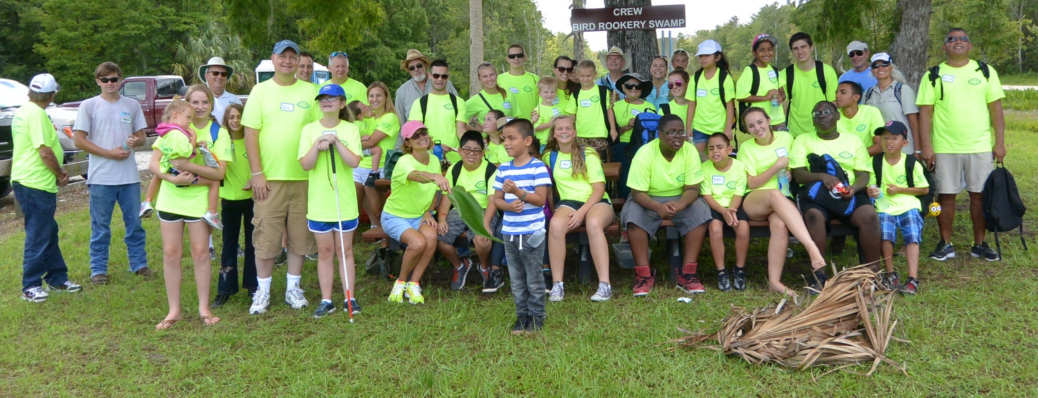 Campers from the 2016 summer program wearing neon green shirts sitting and standing on a bench outdoors.