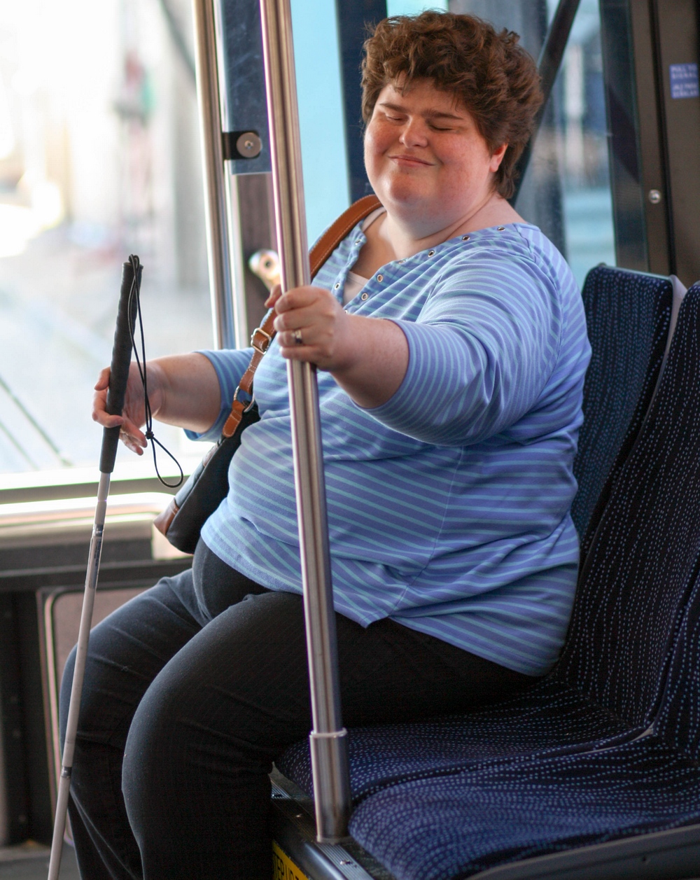 Woman with a white cane sitting on the bus.