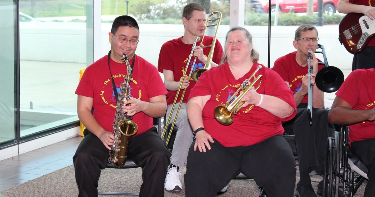 Four musicians wearing red shirts and playing instruments in the Department of Education Turlington Building.