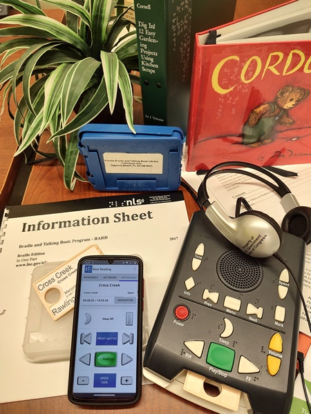 Picture of a digital player, instruction sheet, book cartridge, and BARD mobile on a phone. The book is Cross Creek.