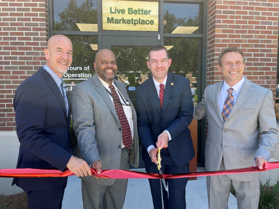 Interim DOE Commissioner Jacob Olivia; DBS Director Robert Doyle; DMS Secretary Todd Inman, and Micro-market manager Patrick Martin, cut the red ribbon in front of the Live Better Marketplace entrance.