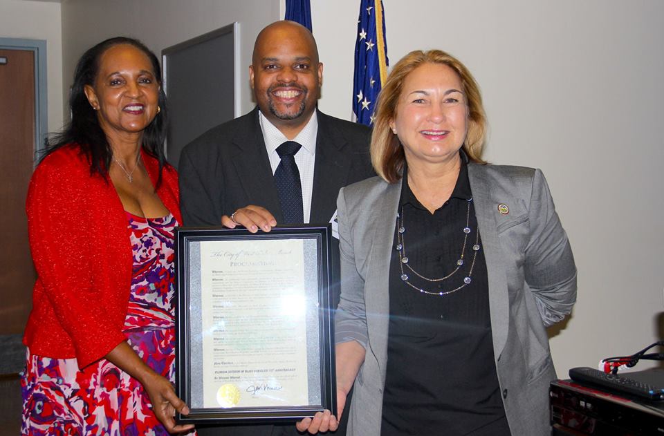 Three people holding up a proclamation from the City of West Palm Beach