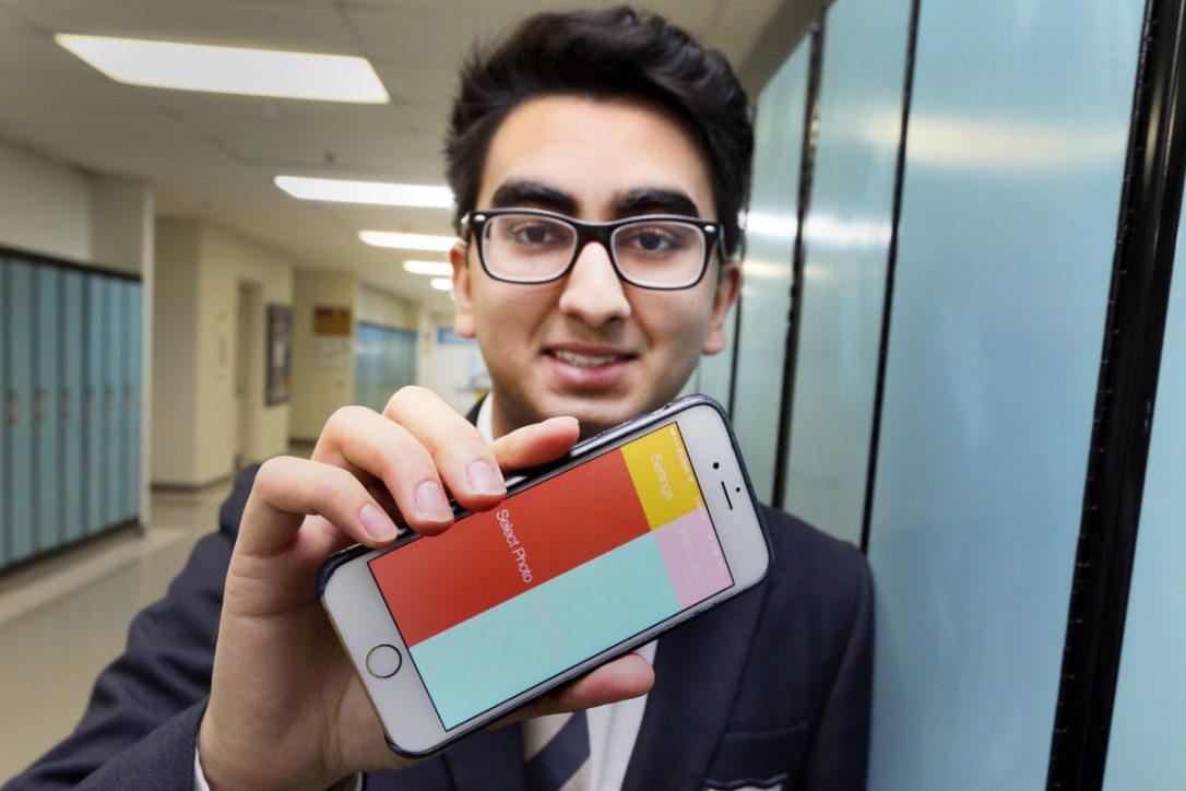 Young male student holds an iPhone while leaning on a locker