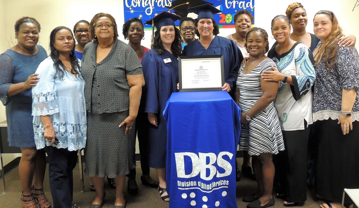 DBS Staff surrounding Jeanne Jenks, who is wearing a blue cap and gown 