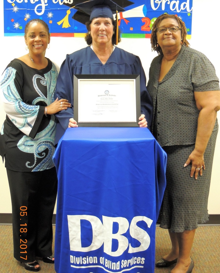 DBS Administrator Michelle Levy, Jeanne Jenks, who is wearing a blue cap and gown and holding up her diploma, and a third woman.