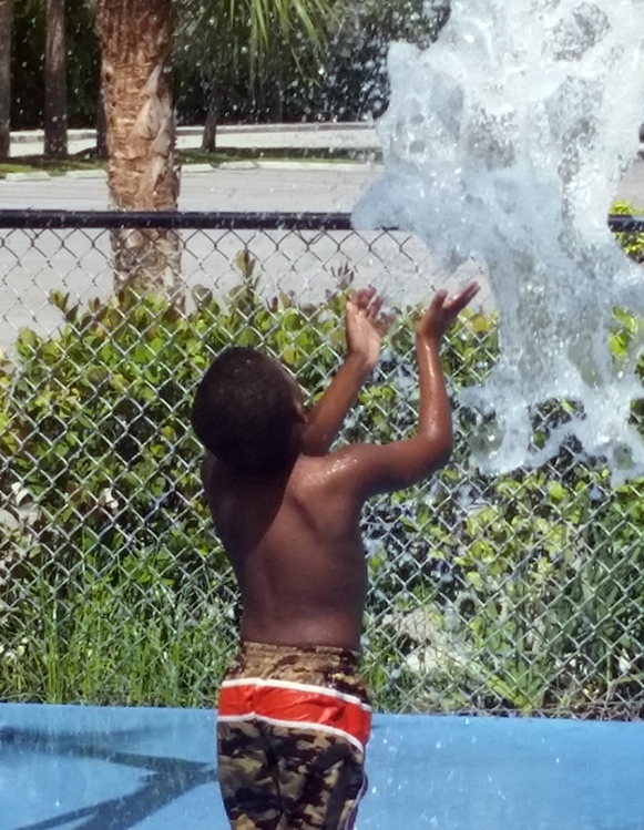 Young male in swim trunks splashing water out of a pool.
