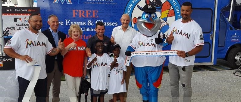 Miami Marlins Baseball players, Virginia Jacko and two students stand in front of the newly-purchased, All-Star branded Mobile Eye Care Unit for Miami Lighthouse's Heiken Children's Vision Program.