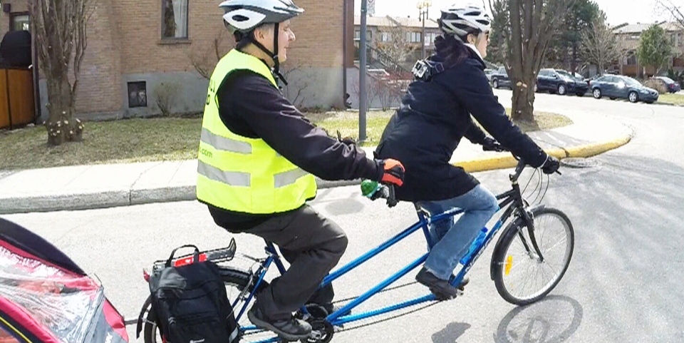 Meals-on-Wheels volunteers Andre Beaudoin and Anick Bergeron ride a tandem bike down the street.
