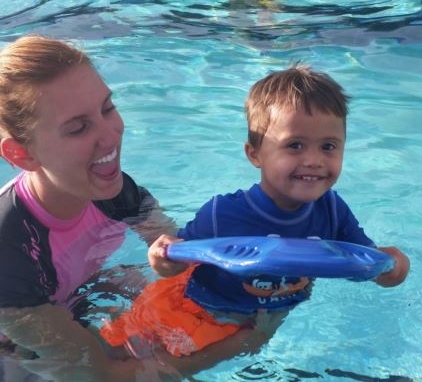 A toddler is being assisted by a woman as he swims on a float in a pool.