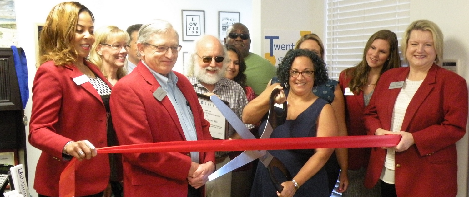 Kim Galban-Countryman, executive director of Lighthouse of the Big Bend, cuts a red ribbon with giant scissors while individuals in red coats look on.