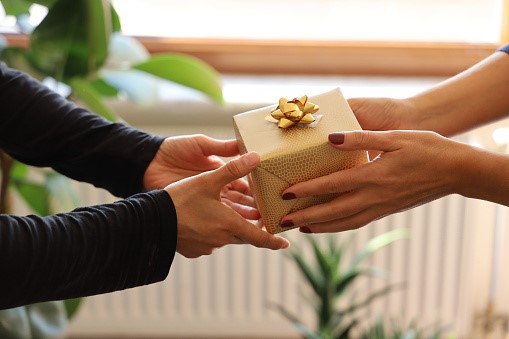 Hands of two people exchanging a gift wrapped in gold wrapping paper.