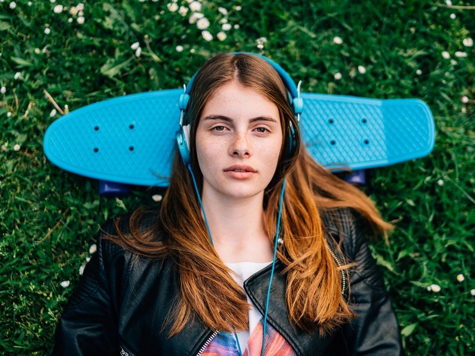 Young lady with headphones and a skateboard.