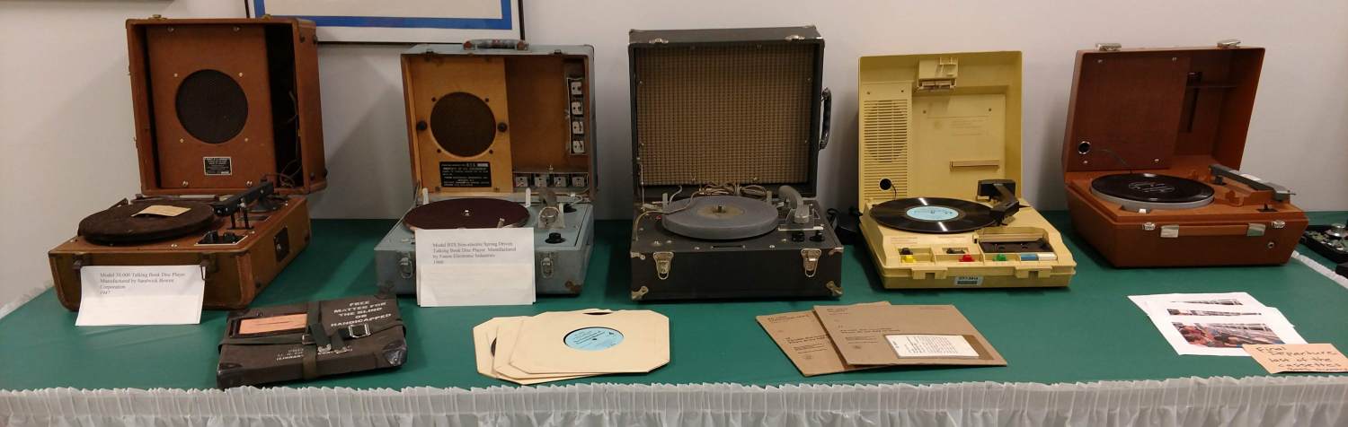 Display table containing five talking book record players and various records.