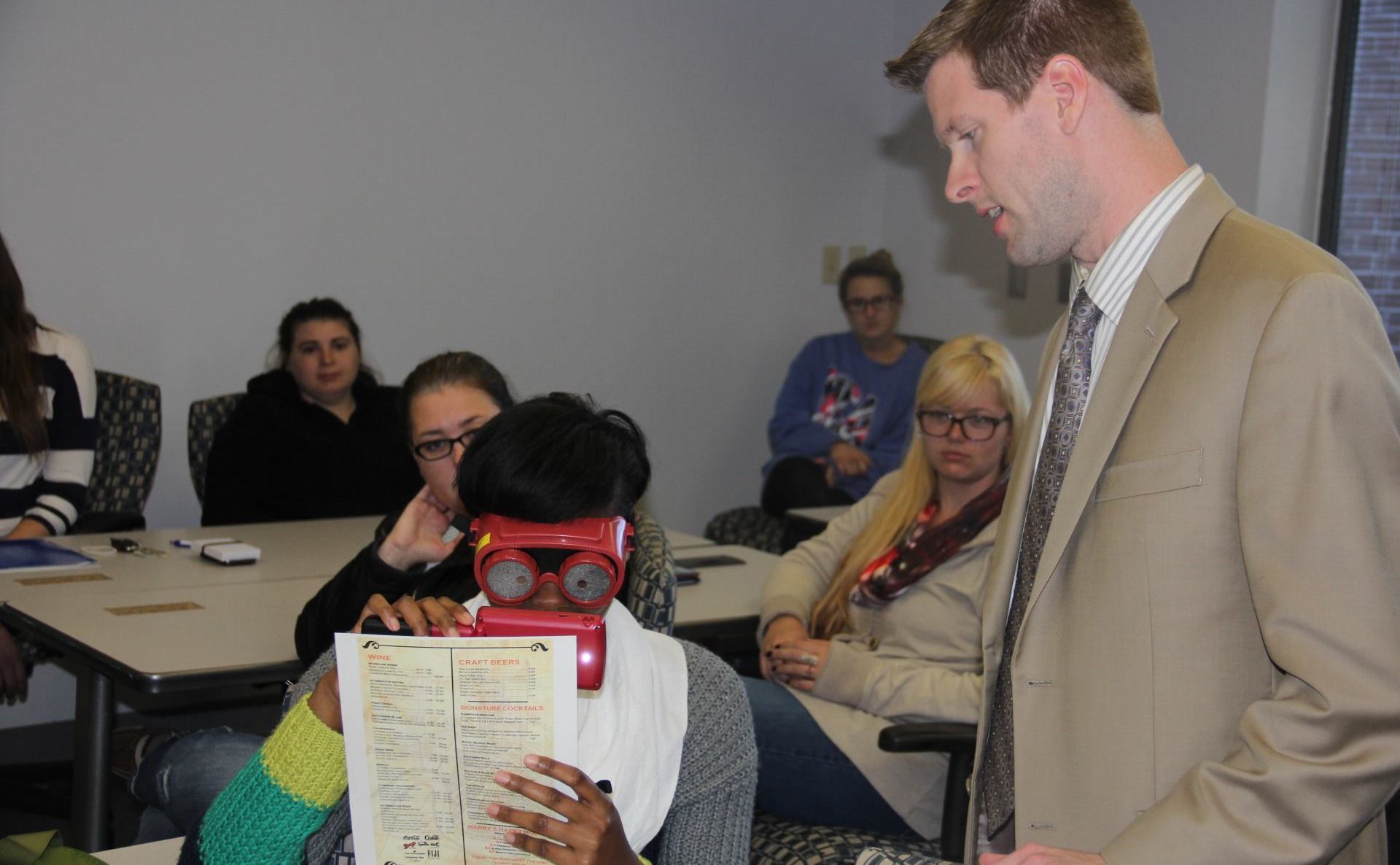See Different attendee using vision simulator glasses and a hand held magnifying aid.