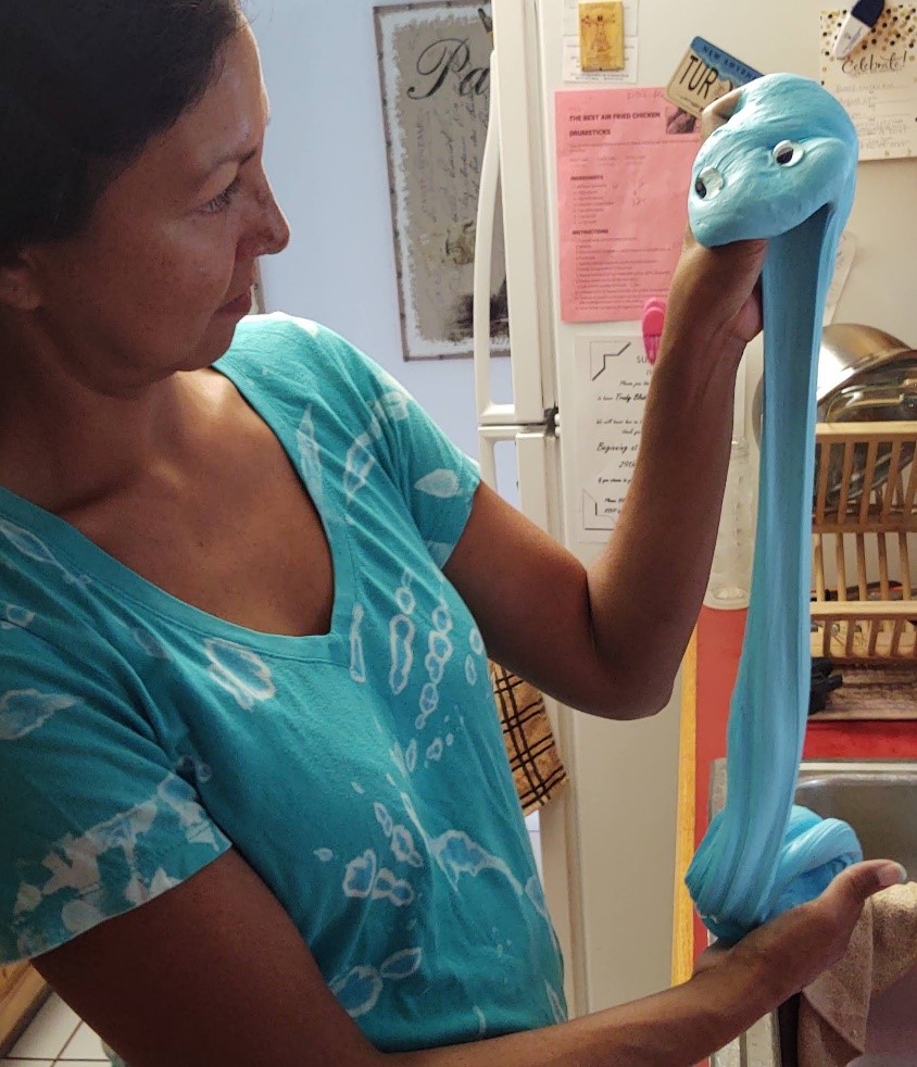 Maureen Dorisinski holding up slime shaped like a worm with googly eyes.